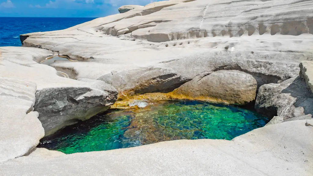 A hole on the bottom of a section of white rock leads to a water hole of emerald and blue clear water  that swimmers can use